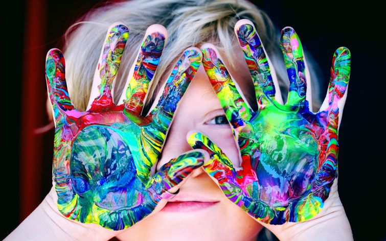 image d'une enfant montrant ses paumes de mains recouvertes de peinture multicolore